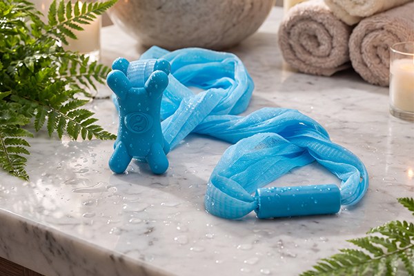 Sea Salt Blue Fähloo exfoliating bathing mesh with its silicone and plastic handles on a marble spa counter