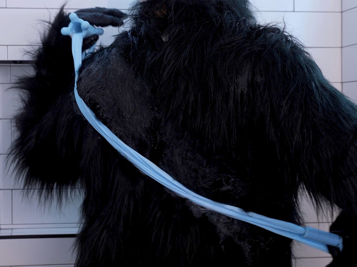 A gorilla holding Fähloo extended diagonally across its back, one handle over the shoulder and one at the hip