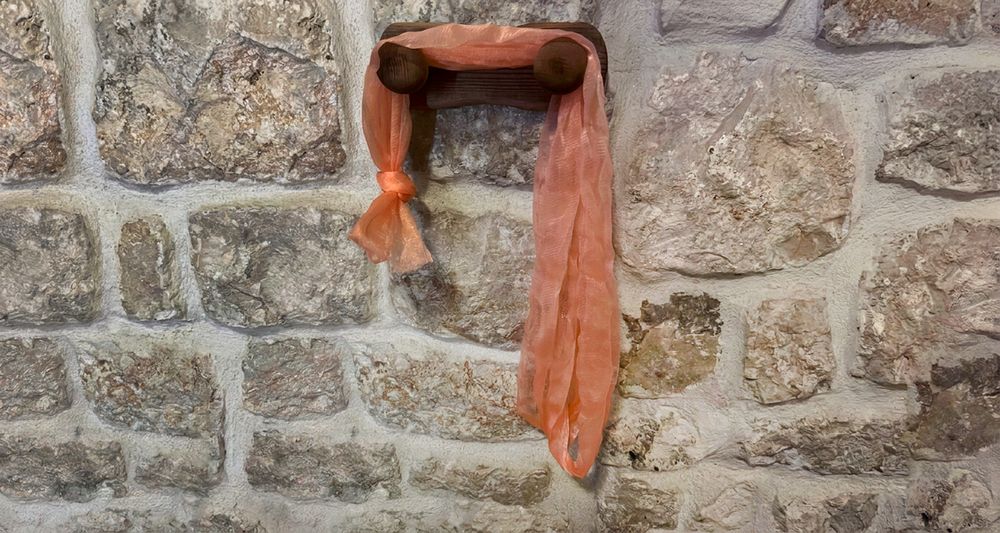 The first homemade Fähloo, a plain coral mesh knotted at one end, draped over a wooden peg on a stone wall in Dubrovnik