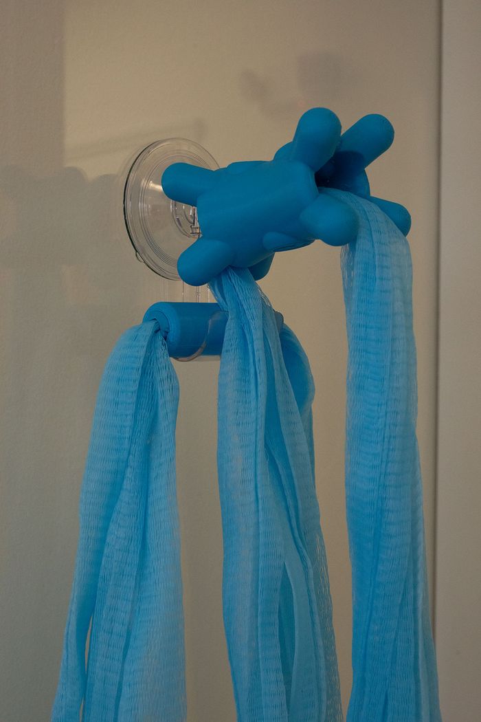The finished Fähloo in Sea Salt Blue, its mesh hanging open to dry from a Shower Valet on the shower wall