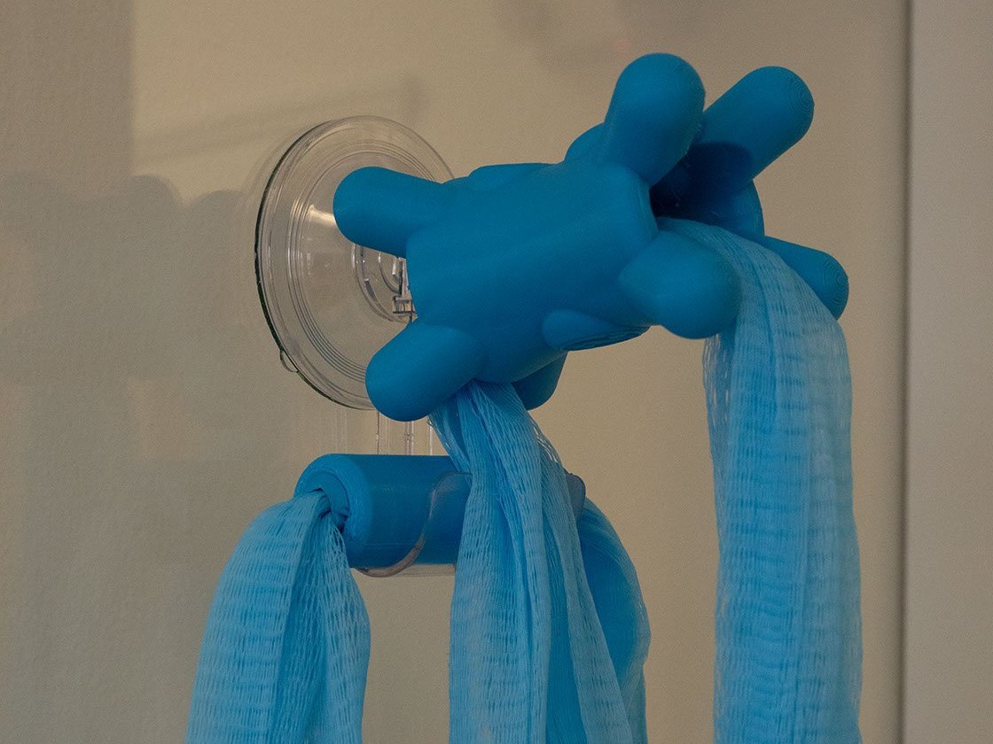 A blue Fähloo hanging by its mesh from the clear Fähloo Shower Valet locking suction hook on a shower wall